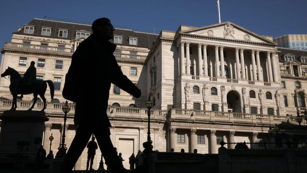 Man in shadow walks in from of the Bank of England building