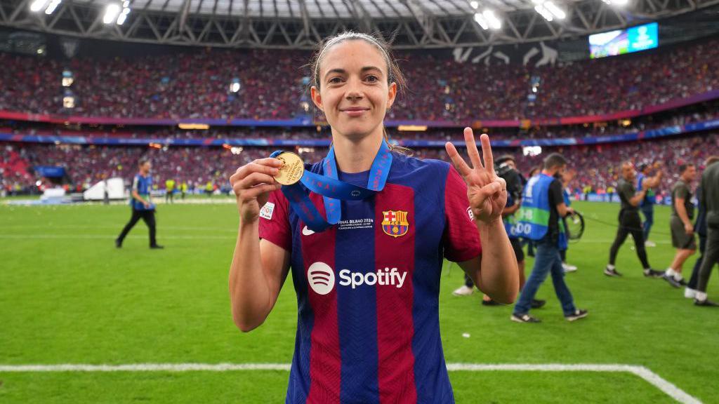 Aitana Bonmati holds her Champions League medal and holds up three fingers