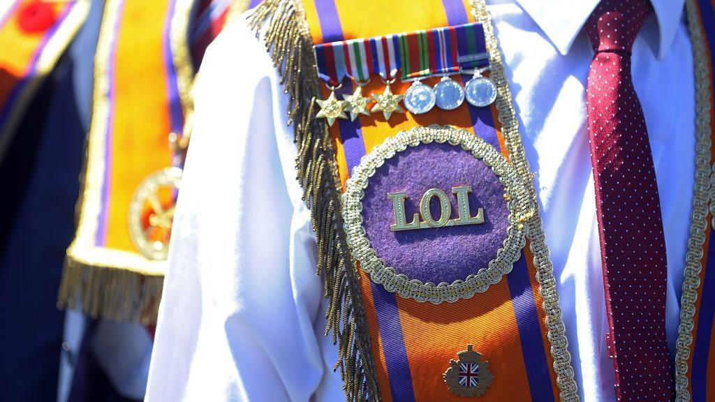 Image shows the torso of a man wearing an Orange Order Sash