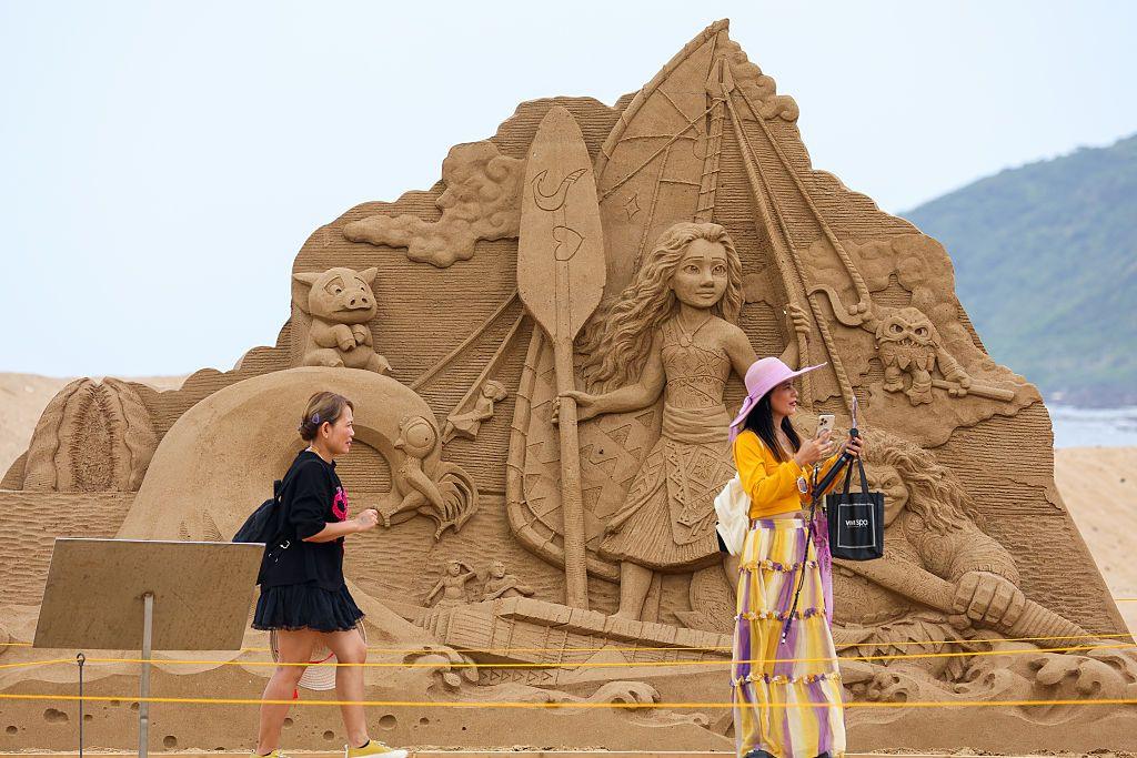 Two women in front of a sand art pyramid of Moana characters