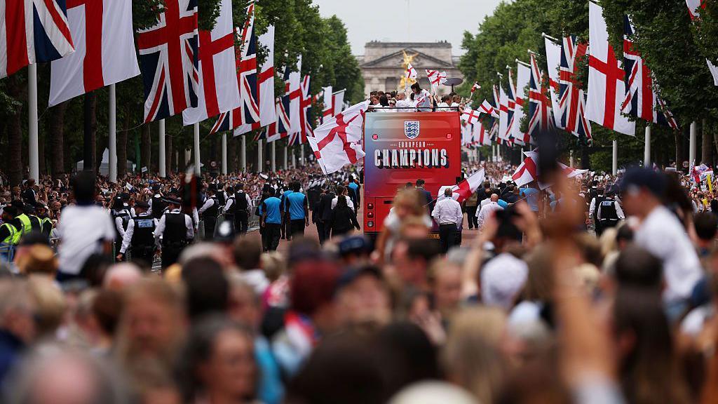 Fans seen from behind as the bus travels up the Mall towards Buckingham Palace.