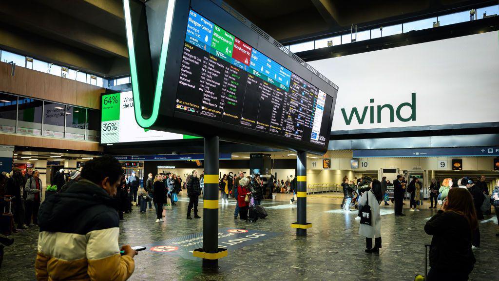 The large advertising display indicates the UK's current use of wind energy, as travellers wait to board trains at Euston Station on January 22, 2024 in London