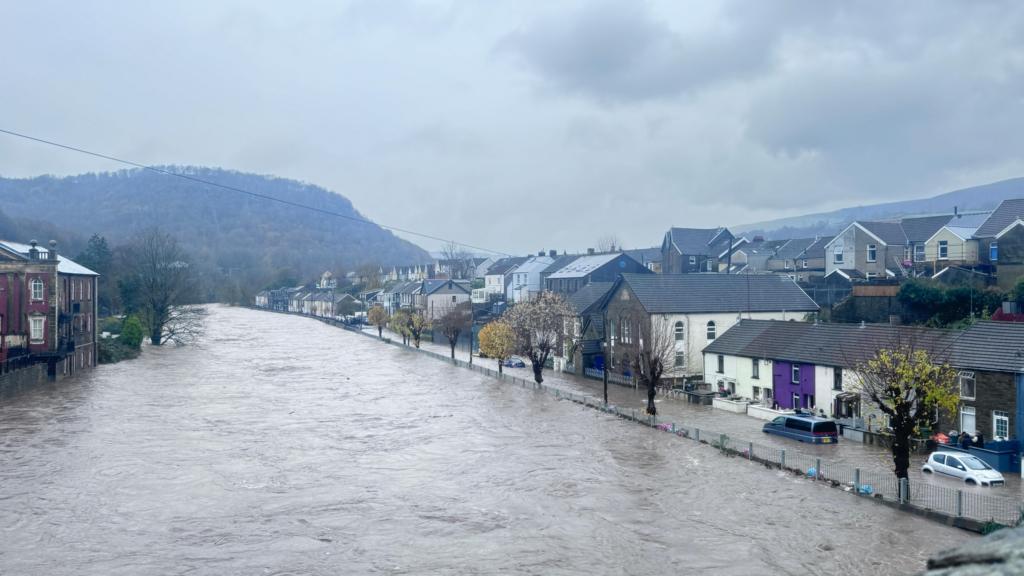 Severe flooding in Pontypridd, the river has burst its banks and floodwater can be seen at a row of houses, with cars submerged 