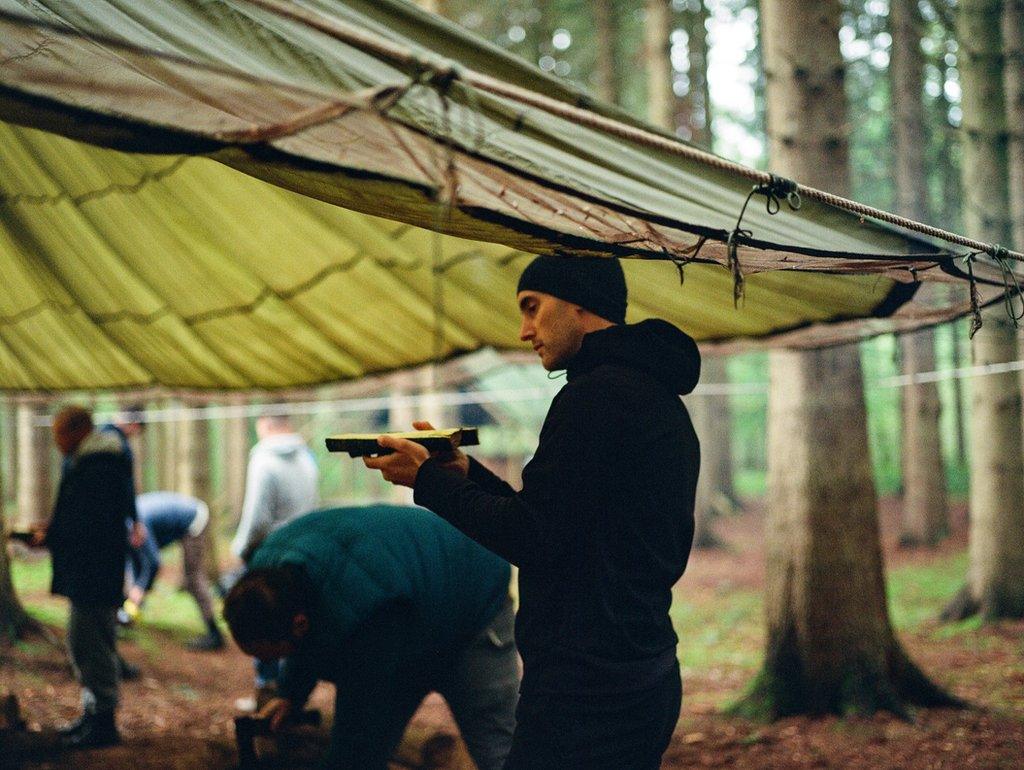 A man examines a piece of woodwork beneath a canopy