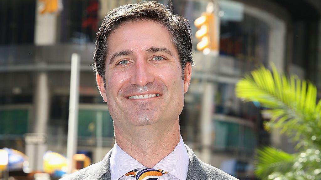 Headshot of Brian Niccol on a street smiling in a suit grey suit and colourful tie