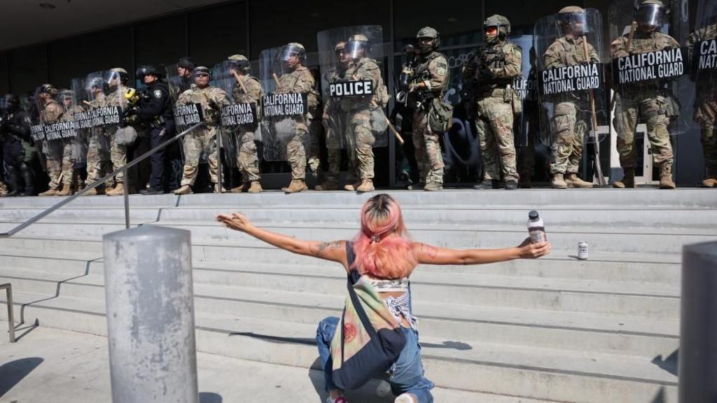 A protester kneels in front of members of the California National Guard