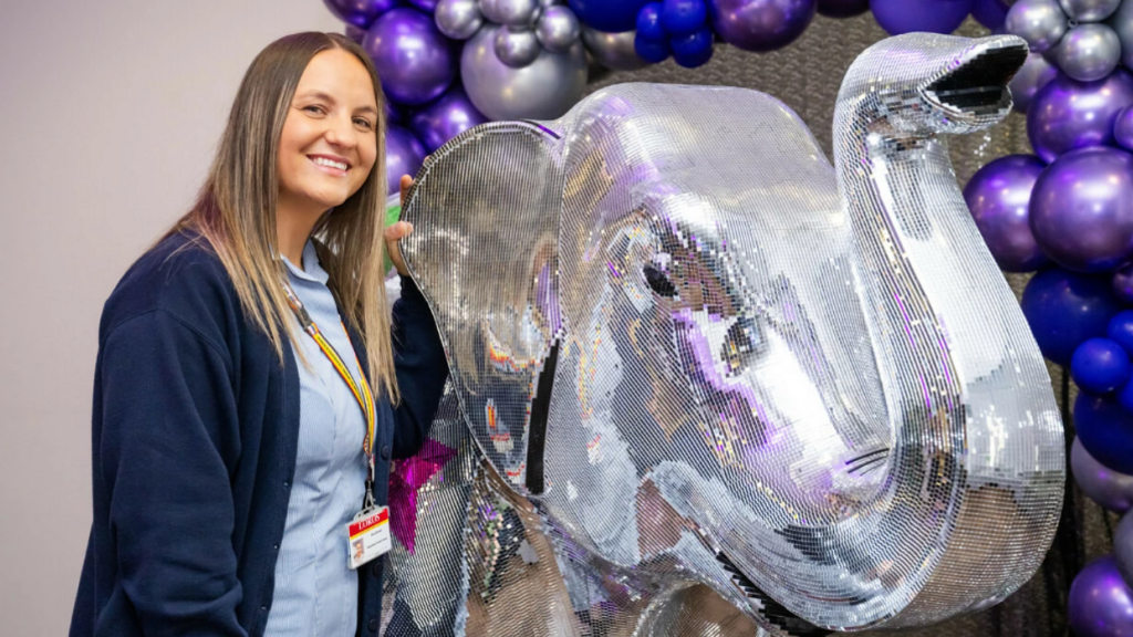 Elephant sculpture covered in mirror pieces next to a woman with brown hair