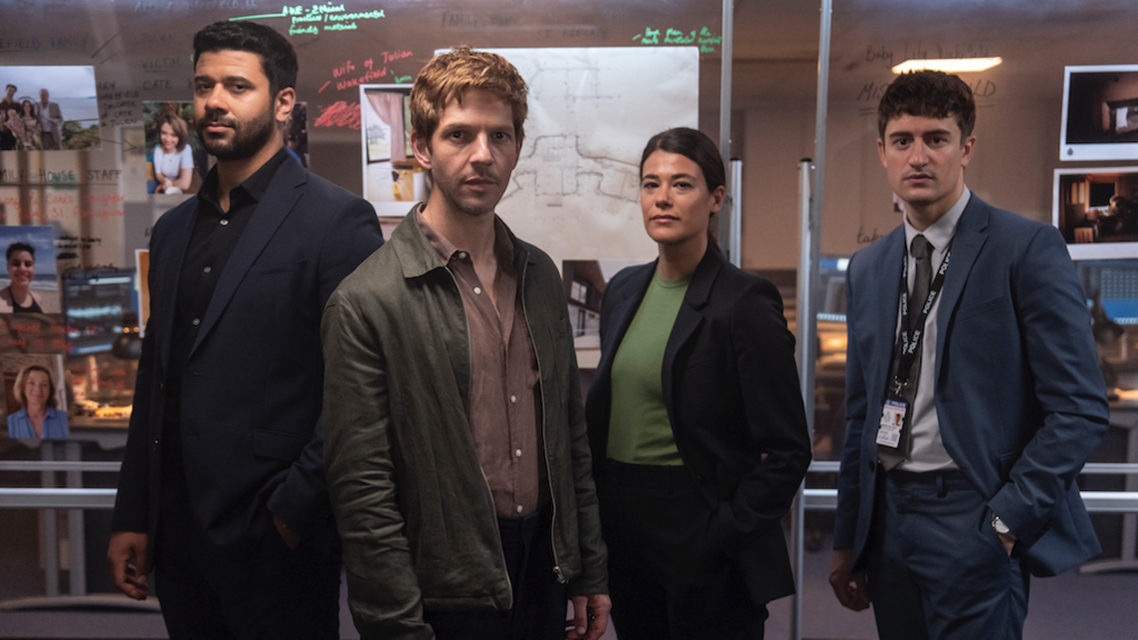 Three men and a woman police detectives, two wearing relaxed work attire and the other two in suit and tie, standing in front of a clear board with writing and images on them.