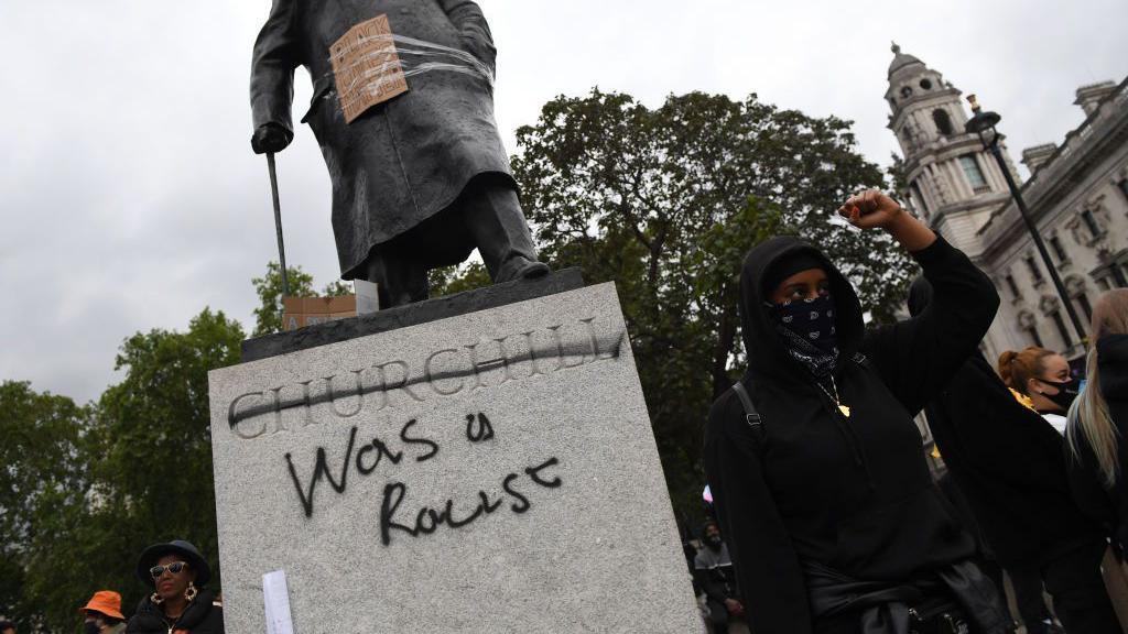 Protesters gathering in Parliament Square Garden around the statue of Sir Winston - his name is crossed out and the words "was a racist" have been added in graffiti.