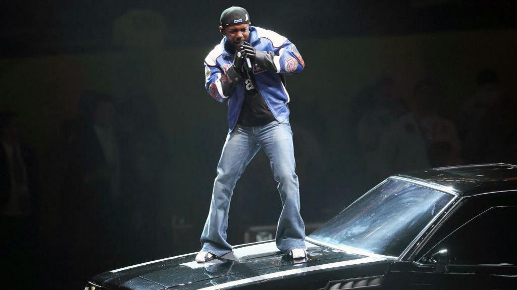 Kendrick Lamar performing atop a car featured on his GNX album cover at his Super Bowl half-time show