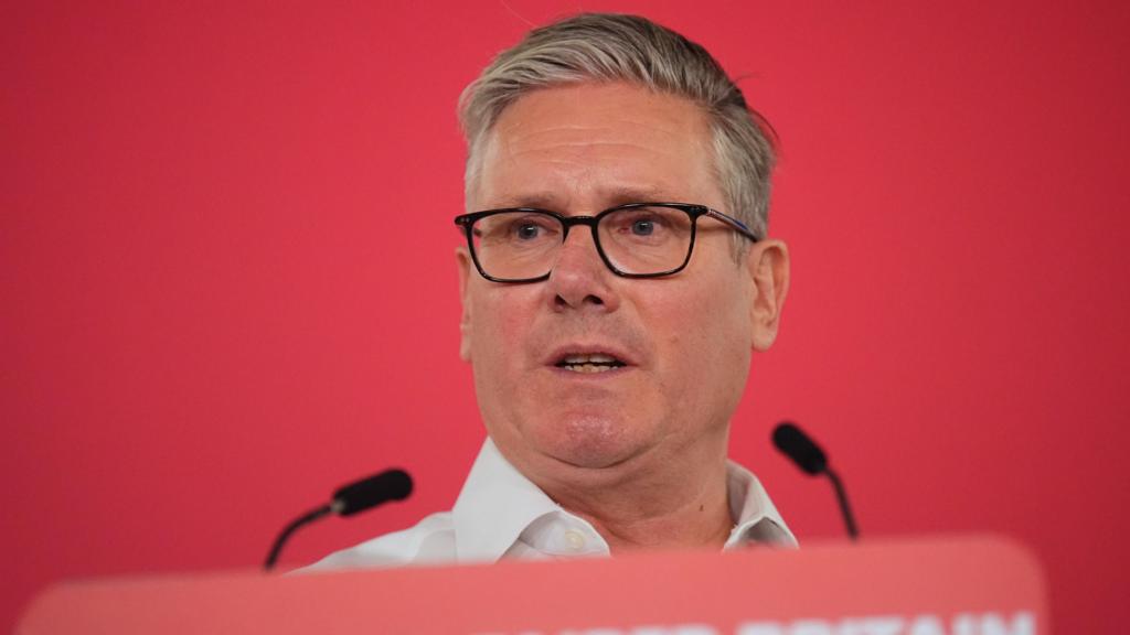 Starmer gestures with right hand while speaking in front of two microphones