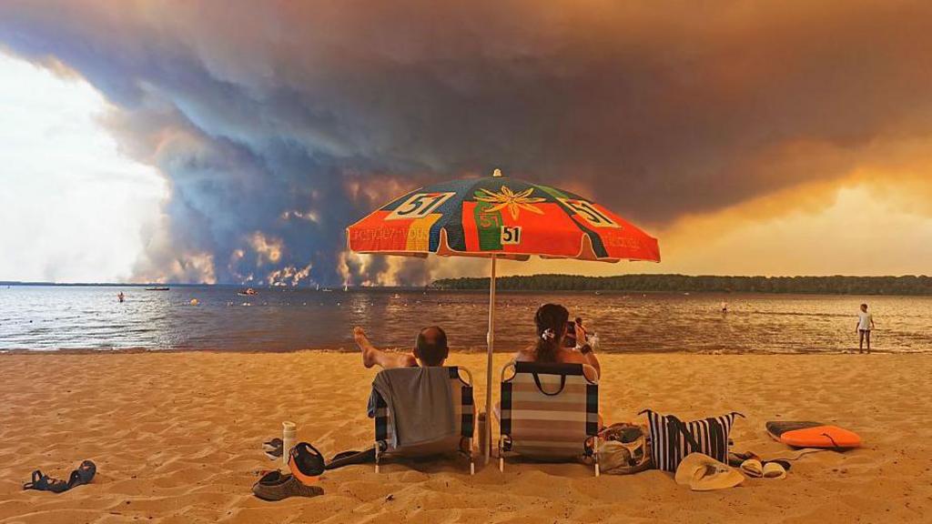 Two people sit in beach chairs as a huge plume smoke fills the sky across the Cap Ferret peninsula in France.