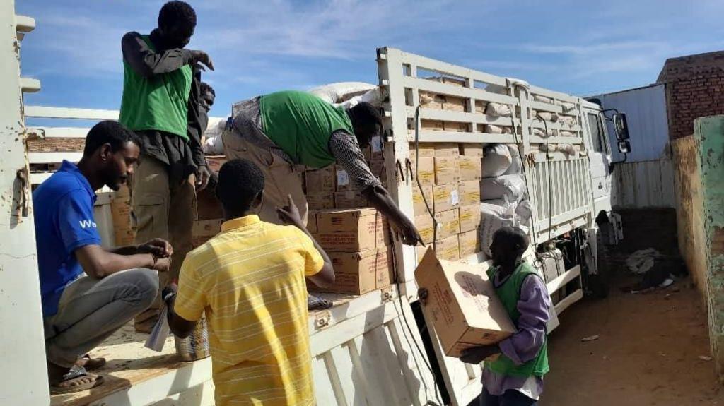 Four men lift cardboard boxes containing aid from a white truck.