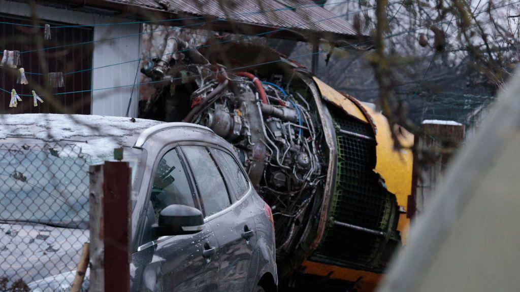 Wreckage of the plane, which looks to be an engine, in a residential area, with a car parked in front of a house