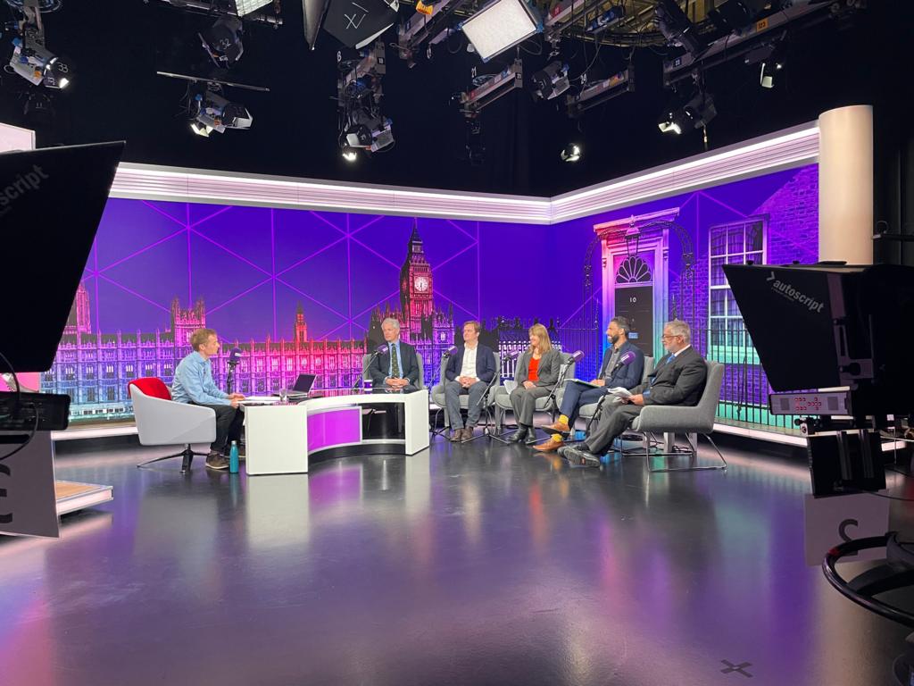 Dan O'Brien and the candidates sitting in a purple studio with cameras in the foreground