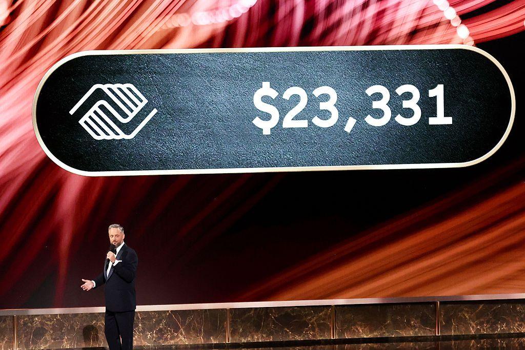 Emmys host Nate Bargatze speaks onstage at the Emmy Awards with a large sign behind him saying $23,331 next to a logo for the Boys and Girls Club of North America.