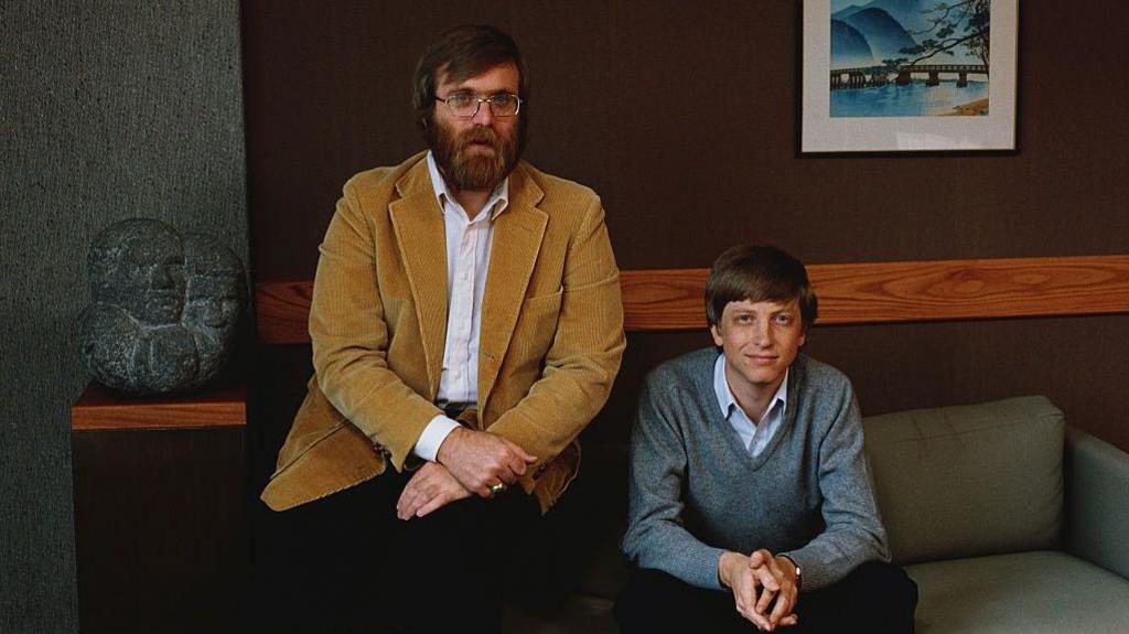 Paul Allen and Bill gates sitting on a sofa and looking at the camera