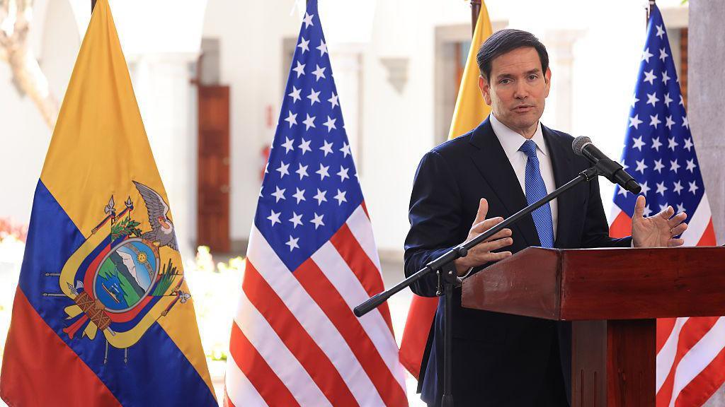 Marco Rubio stands in front of Ecuador and US flags