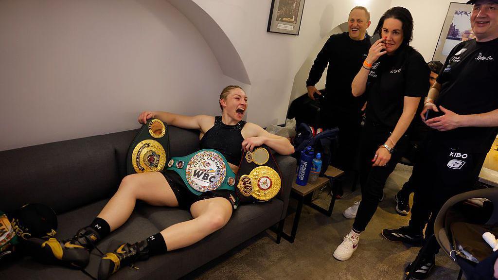 Lauren Price jokes with her team as she relaxes in her dressing room with her belts after beating Natasha Jonas during the all women's boxing card at the Royal Albert Hall on March 7th 2025 in London, England