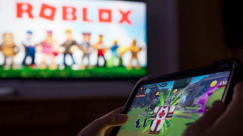 child playing roblox in front of roblox sign