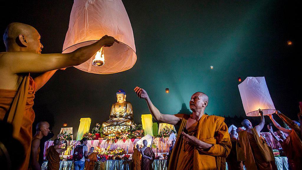 Buddhist monks light and release paper lanterns outside a temple.