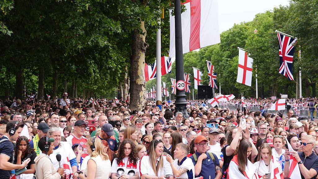 Crowds of people line the mall with St George's Cross and Union flags seen hanging