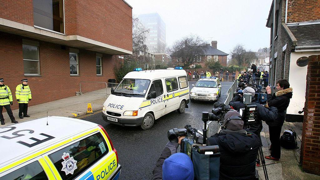 Një furgon policie që mbante Steve Wright mbërrin në Gjykatën e Magjistraturës në Ipswich. Një makinë policie është përpara furgonit, dhe një tjetër pas tij. Një grup i madh mediash është vendosur pas barrierave metalike me shumë kamera të drejtuara nga rruga.