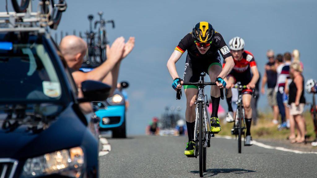 A rider cheered on by his support vehicle staff