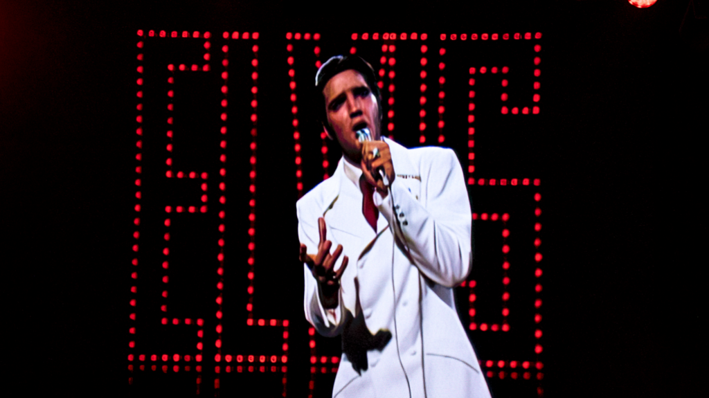 Elvis Presley in a white suit and a microphone in one hand