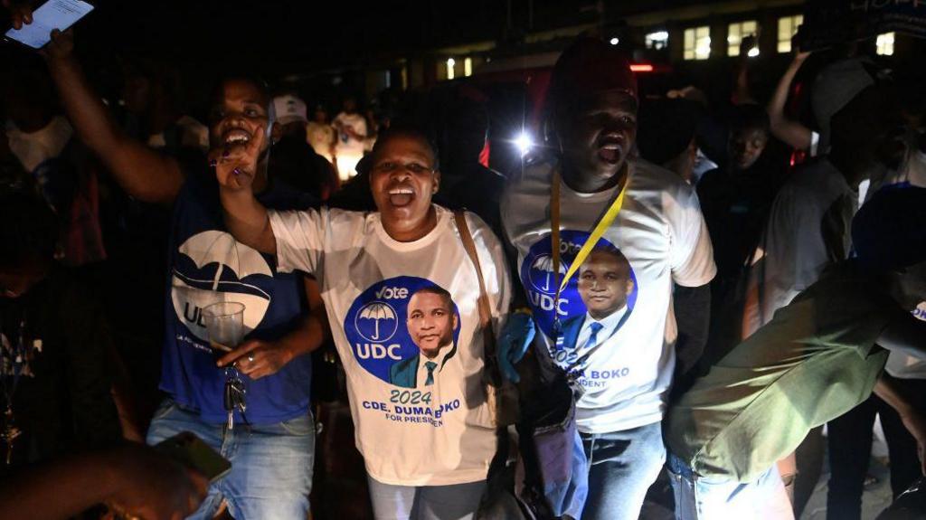 People wearing UDC T-shirts raising their arms in celebration at night.