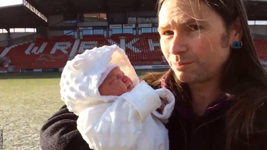 Adam Phillips with his newborn daughter Tanwen standing in the centre circle at the Racecourse Ground