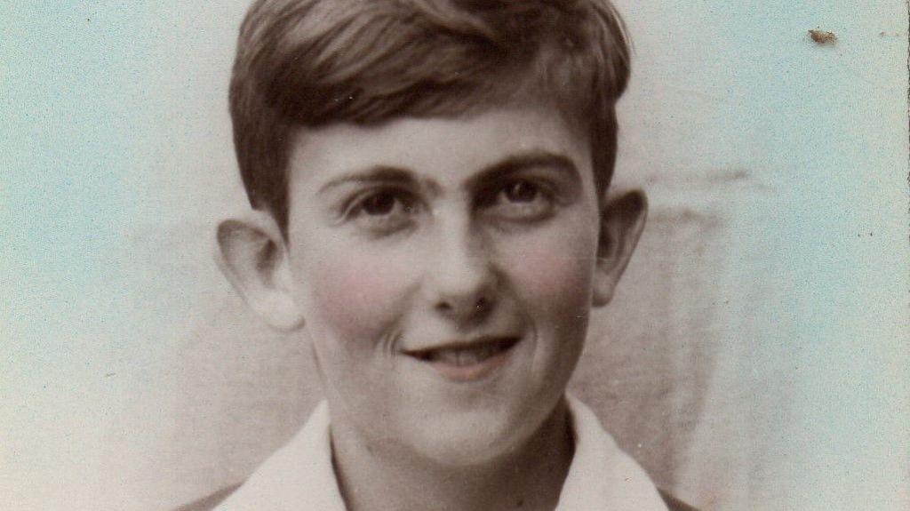 Black and white photograph of a smiling young boy with short dark hair wearing a white shirt and a blazer.