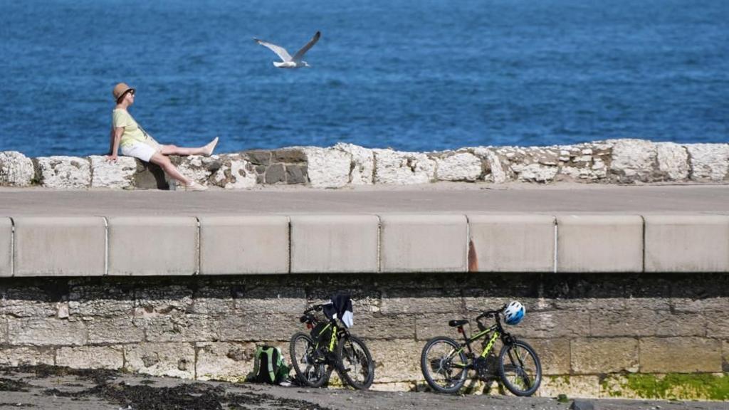 A woman enjoys the sun in Carrickfergus, Northern Ireland, during the hot weather. Temperatures could reach 32C in parts of central and southern England on Friday