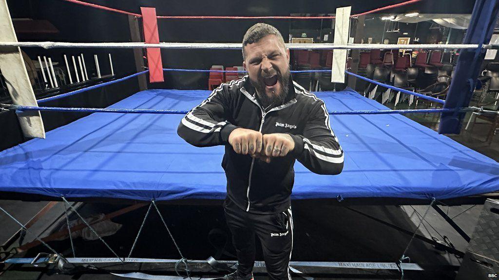 Wrestler Zak Knight standing in front of a wrestling ring