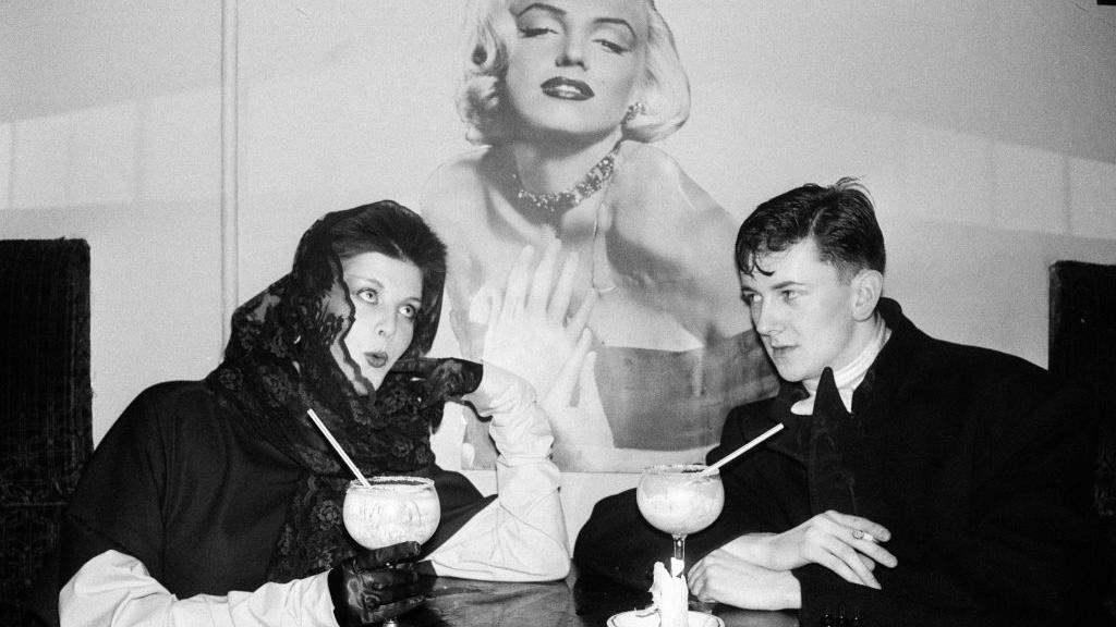 Woman and man with cocktails sitting in front of a picture of Marilyn Monroe 