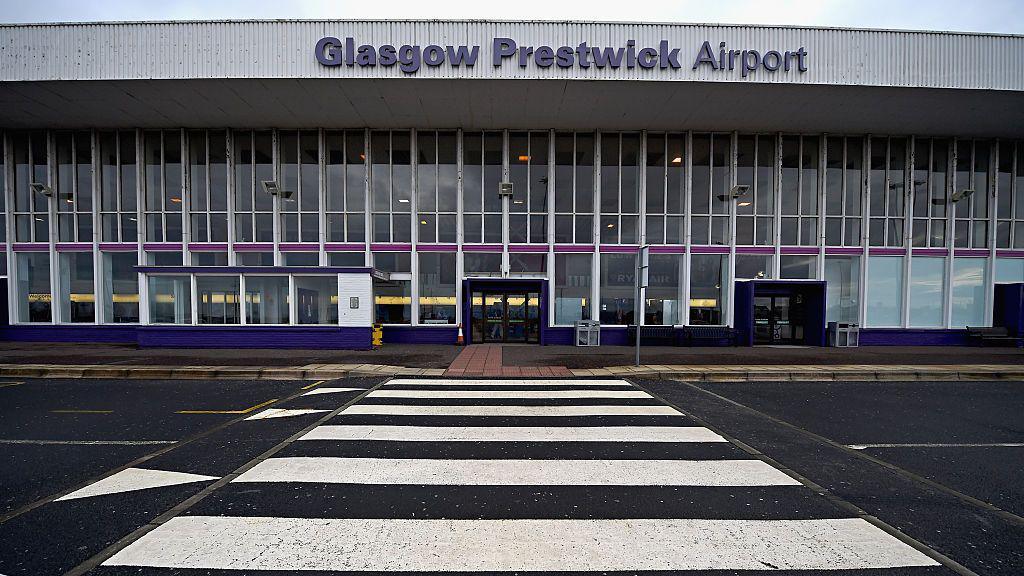 The entrance to a large airport building, with the view coming from across the street. The sign says Glasgow Prestwick Airport