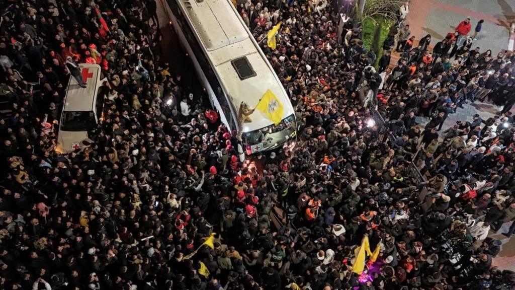 Aerial view of large crowd surrounding a bus as people wave flags