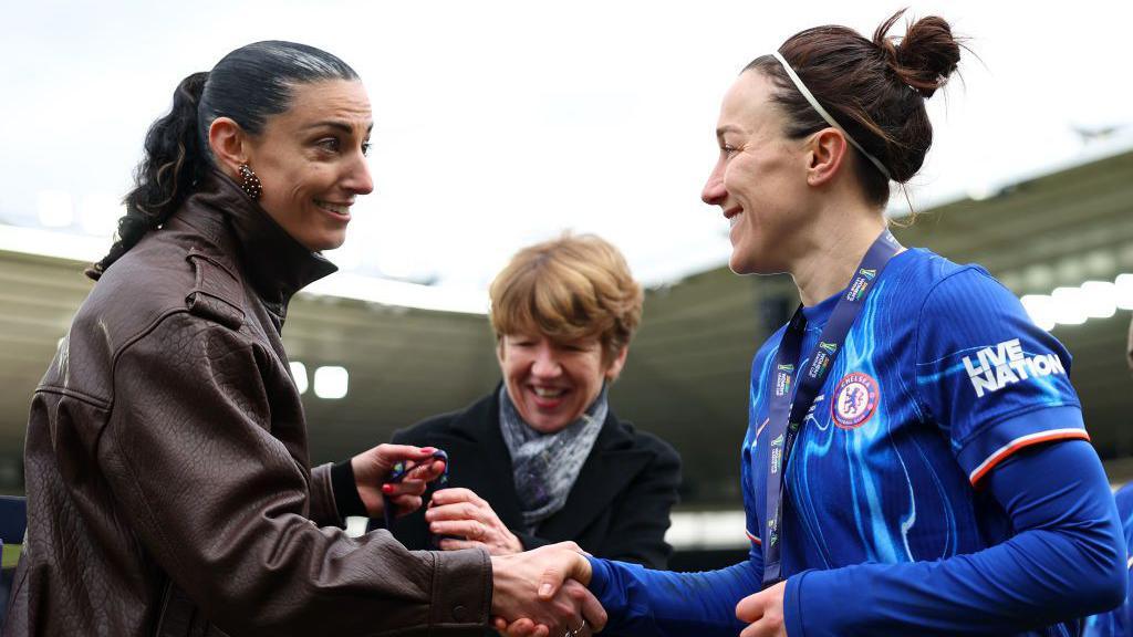 Nikki Doucet shaking hands with Lucy Bronze in 2025