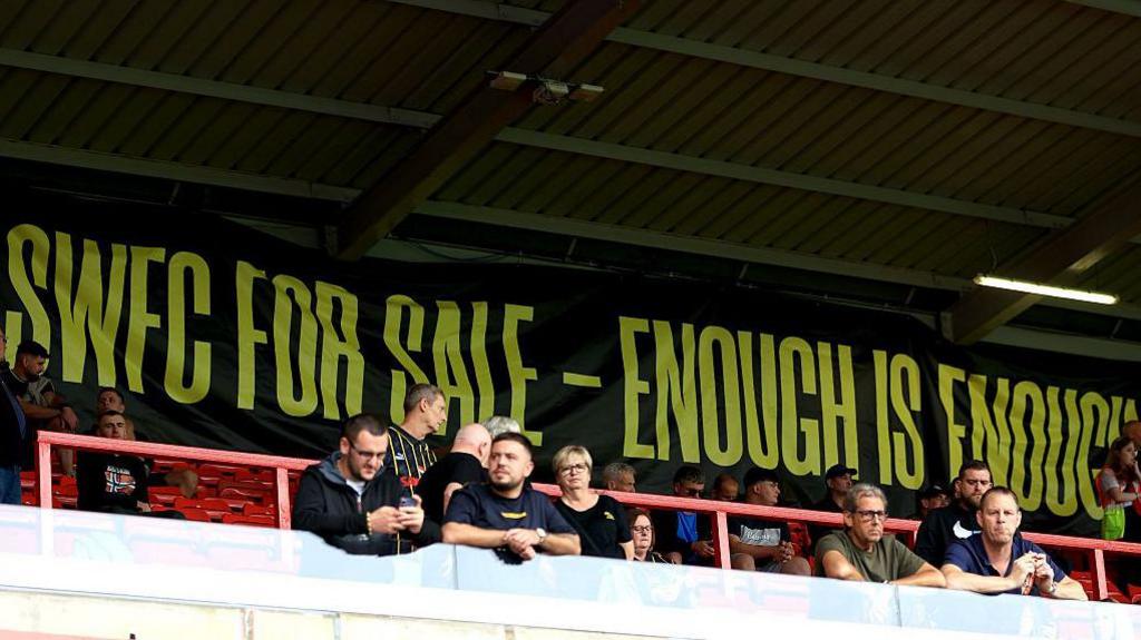 Sheffield Wednesday supporters stand in front of a banner that reads 'SWFC for sale - enough is enough'