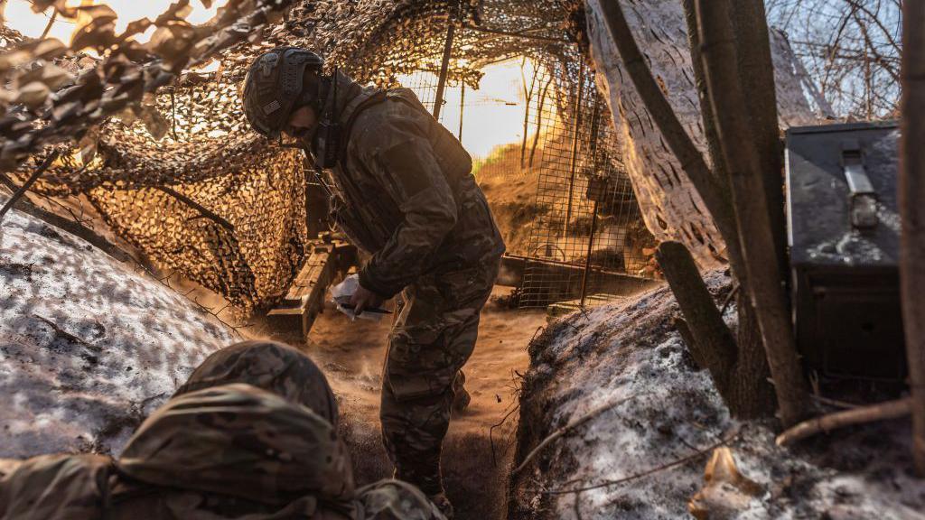 A Ukrainian national guard soldiers stand in a trench under camouflage netting amid snowy conditions as they fire the Soviet D-20 artillery in the direction of Pokrovsk, Ukraine 