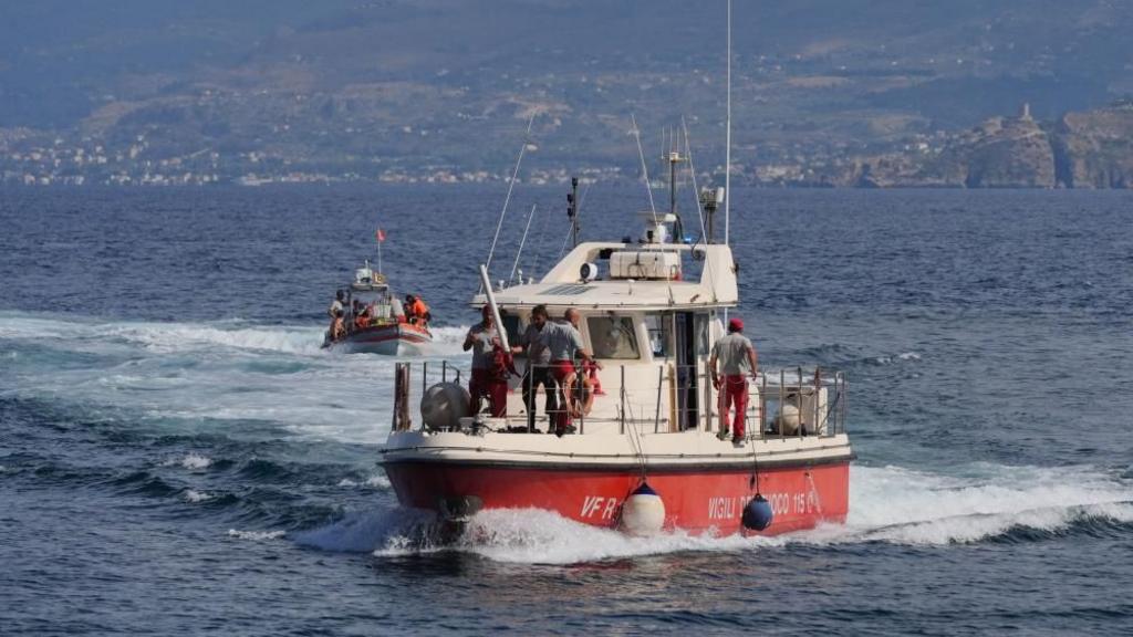 Rescuers in a white and orange boat survey the area where a luxury yacht sank in the daylight.