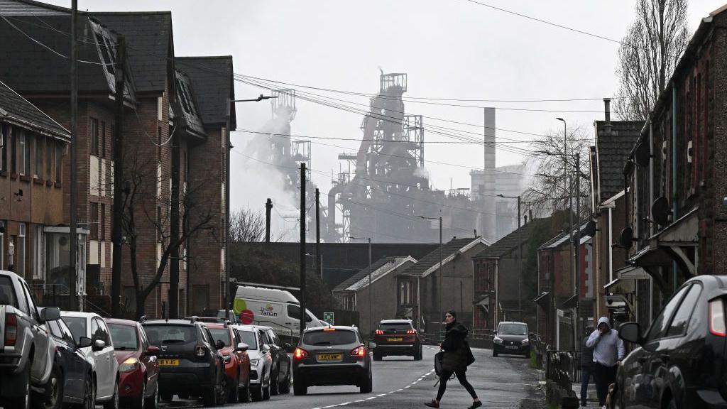 A person walks across the road in a residential neighbourhood near to the Tata Steel Port Talbot integrated iron and steel works in south Wales on February 9, 2024. In the dim light of a pub in the steel producing Welsh town of Port Talbot