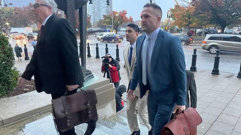 Brett Hankison in blue suit carrying brown briefcase walks up courthouse steps next to a man in a dark suit and a man in a cream suit