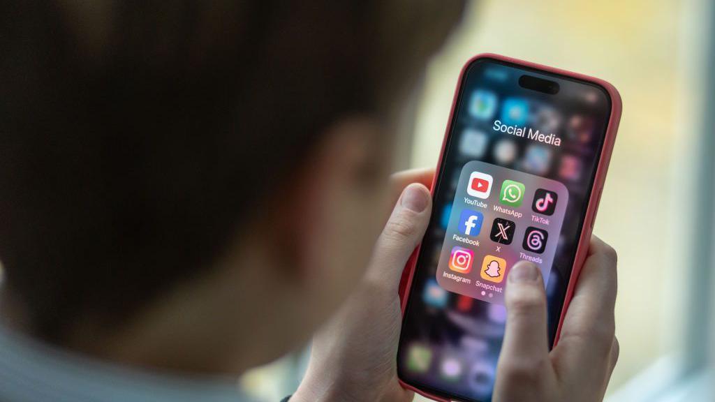 In this photo illustration a 12-year-old boy looks at an iPhone screen showing various social media apps including TikTok, Facebook and X