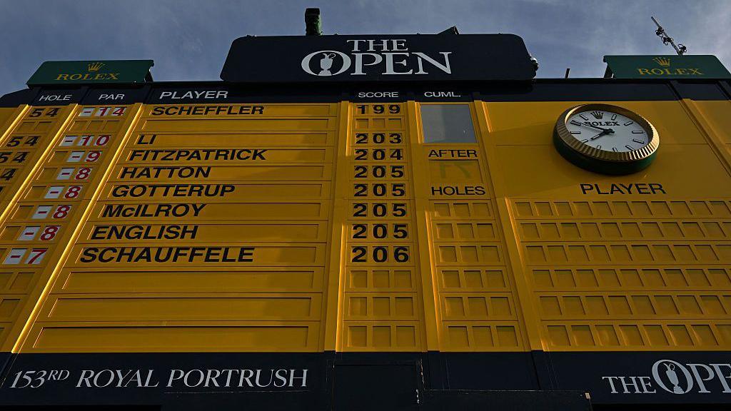 A close up on the leader board at The Open which was held at Royal Portrush. The large yellow and black board shows a clock and Scottie Scheffler's name at the top.