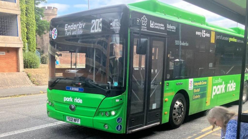 A Park and Ride bus service at a bus stop in Leicester. The single deck bus is bright green with a sign that reads 'Enderby Park and Ride 203' on the front.