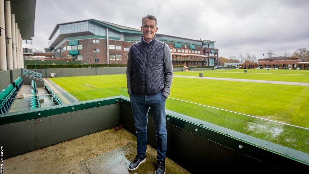 Neil Stubley, head of courts and horticulture, stands in front of Centre Court smiling