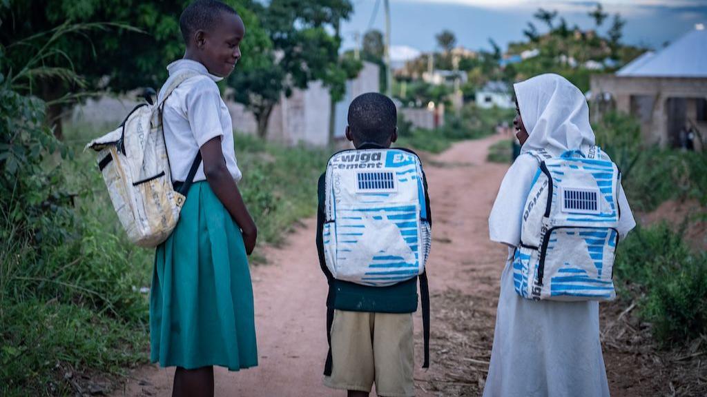 Three children walking to school with solar powered backpacks on