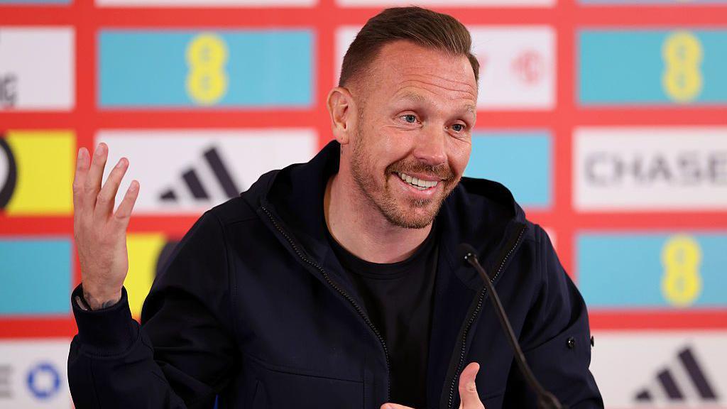 Craig Bellamy holds up his hands and speaks into a microphone