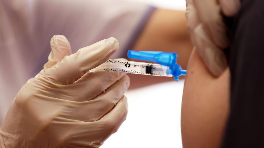 A close-up photo of a gloved hand injecting a vaccine into a person's arm.